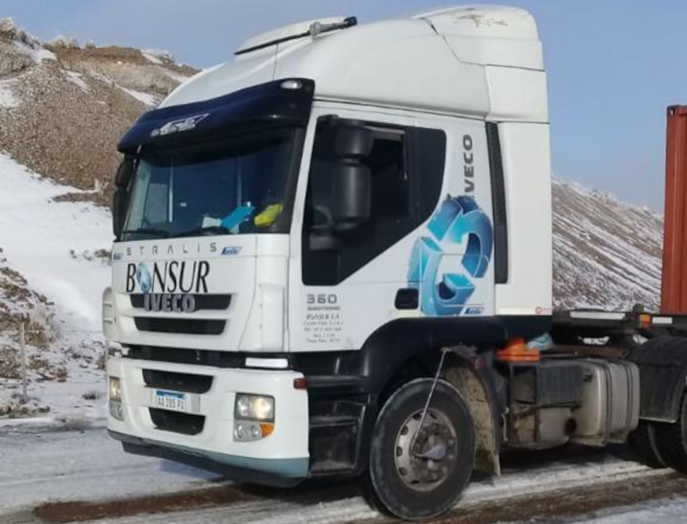 Camión blanco IVECO Stralis de la empresa Bonsur, equipado con un logo circular distintivo y el número 360. El vehículo se encuentra circulando por una ruta montañosa en condiciones invernales.